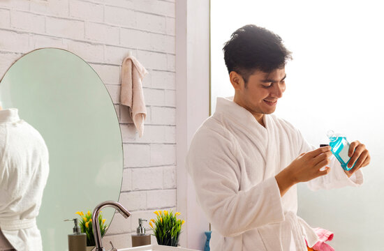 Smiling young man in bathrobes pouring mouthwash in bathroom