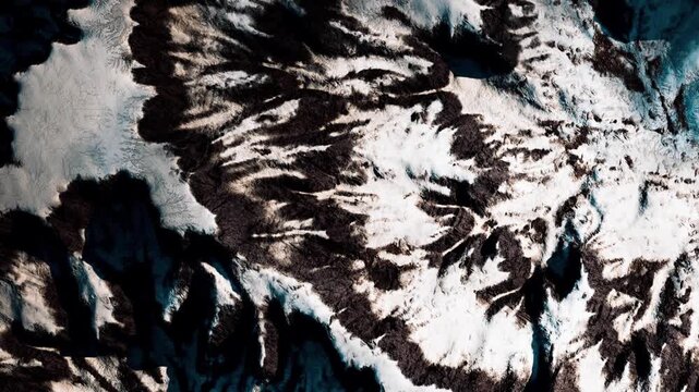 The scene shows a mix of snow and dark rock in a mountain area. The view is from above, highlighting the patterns formed by snow and terrain. This image captures the natural beauty of the landscape.