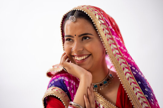 Close-up portrait of a smiling Rajasthani young woman with hand on cheek against white background