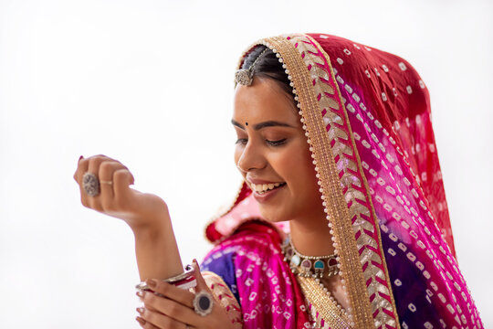 Close-up portrait of Rajasthani young woman looking at bangles against white background