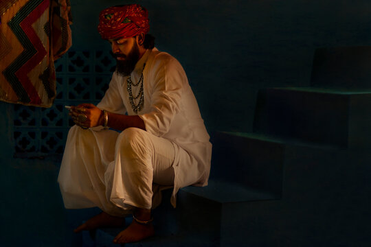 Portrait of Rajasthani man using mobile phone while sitting on stair at home