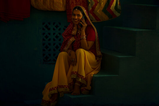 Portrait of Rajasthani woman talking on mobile phone while sitting on stair at home