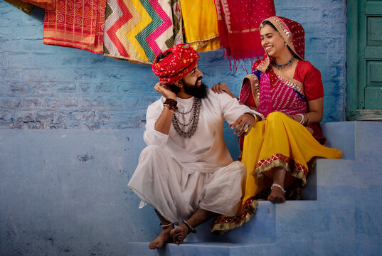 Rajasthani couple sitting on stairs sharing a light moment,as the husband plays ektara