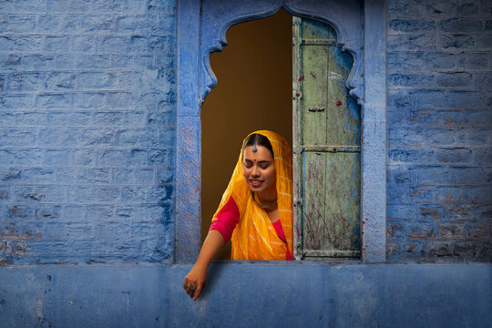 Rajasthani young woman looking down and pointing through window