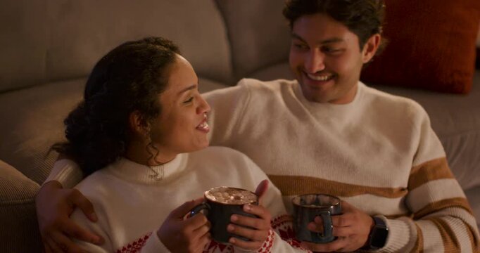 Couple sitting on couch wearing knit sweaters, holding mugs with spoon, chat sparking smiles