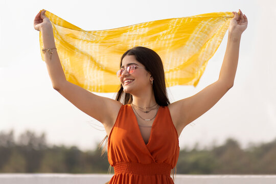 Beautiful young lady standing on the beach and holding a yellow scarf in the wind