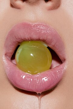 Woman's pink lips with glossy lipstick holding green grape. Close-up of female mouth with fruit. Beauty and taste concept.