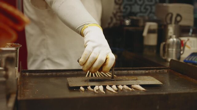 Street food in China, cook grilling octopus or squid tentacles, closeup view. Enjoy traditional Chinese cuisine, seafood made on grill, fast food restaurant in street, show kitchen, tasty meals