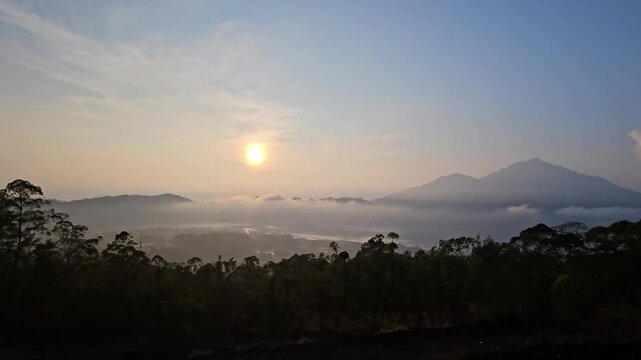 Wide cinematic shot of a golden sunrise over Mount Batur caldera with low clouds and misty lake in Bali, Indonesia. Beautiful morning nature video.
