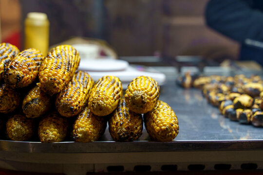 grilled corn served on metal tray in food stall with condiment bottle warm and inviting side view close-up street food market yellow brown commercial natural light clean background copy cop.