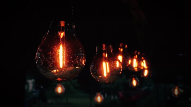 Close-up of string lights with warm vintage Edison light bulbs glowing brightly against a dark night background, creating a cozy and atmospheric ambiance.