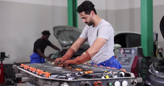 Professional EV technician inspecting high-voltage battery electrical connections inside a modern electric vehicle service center.