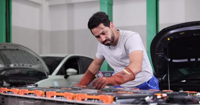 Professional EV technician inspecting high-voltage battery electrical connections inside a modern electric vehicle service center. 