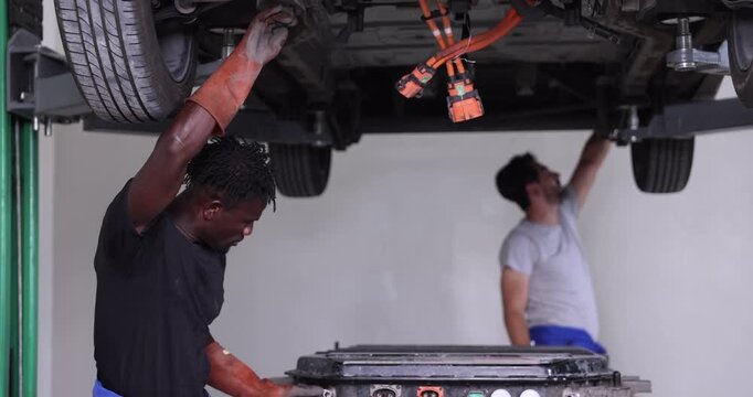 Professional EV technicians reconnecting high-voltage battery connectors beneath a lifted electric vehicle during battery pack reinstallation.