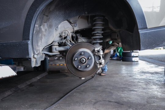 Exposed car suspension, brake disc, and shock absorber on an auto repair shop lift. Professional vehicle maintenance, undercarriage safety inspection, and fixing in a mechanic garage