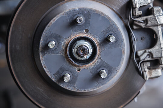 Close-up view of a car brake caliper, brake disc rotor, and wheel studs. Essential automotive parts exposed during a vehicle safety inspection and maintenance service in a mechanic shop