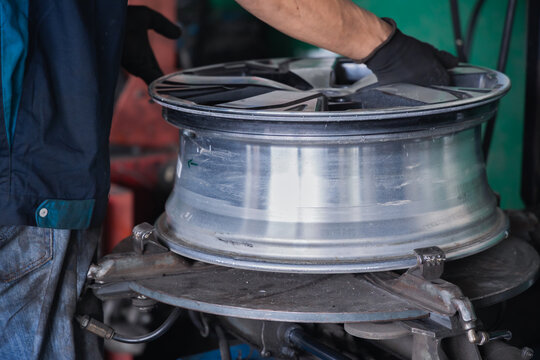 Hands of a mechanic placing a bare aluminum alloy wheel onto a pneumatic tire changer machine. Professional wheel mounting and automotive maintenance in a specialized auto repair shop