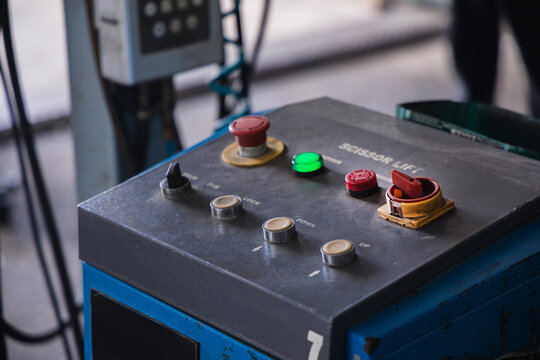 Scissor lift control panel with emergency stop button and operating switches. Industrial heavy machinery and safety equipment in a professional auto repair garage