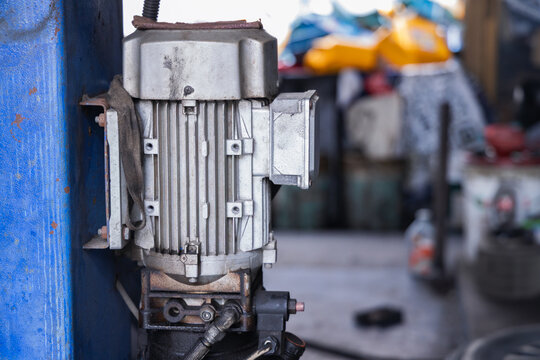 Electric motor and hydraulic pump system attached to a heavy-duty car lift post in an auto repair shop. Industrial machinery and garage equipment for professional vehicle maintenance