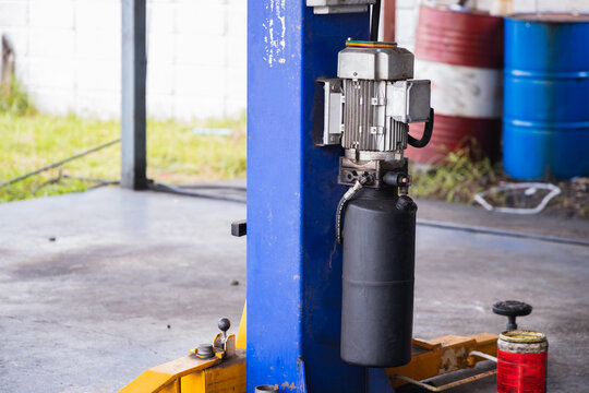 Electric motor and hydraulic pump system attached to a heavy-duty car lift post in an auto repair shop. Industrial machinery and garage equipment for professional vehicle maintenance