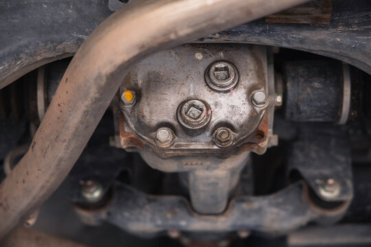 Car rear differential and drive axle exposed on an auto repair lift. Vehicle undercarriage drivetrain inspection and gear oil maintenance in a mechanic garage