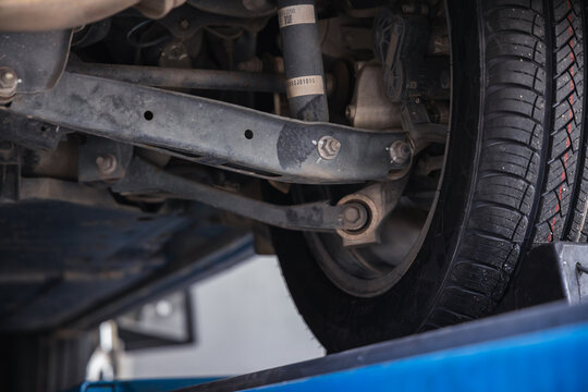 Car suspension system featuring a lower control arm and shock absorber. Vehicle undercarriage inspection and professional auto repair maintenance on a garage lift