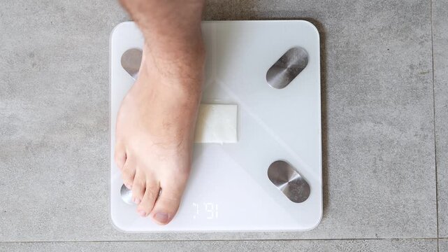 Close-up of a man stepping onto a digital bathroom scale as the display changes from zero to the final weight. Daily weight monitoring and healthy lifestyle concept.