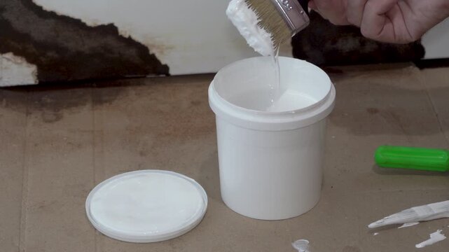 Painter dips brush into white paint, Dipping paint brush into white paint bucket close up
