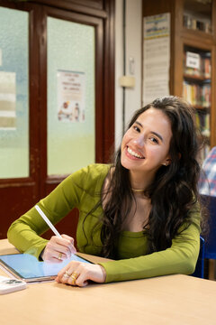 Young female student smiling, drawing on a tablet with a stylus in a library setting