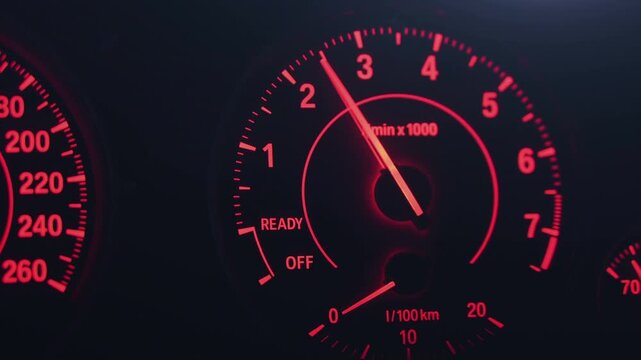Close-up of a red illuminated car tachometer as the needle rises and falls on a dark dashboard, showing engine revs and instrument panel details at night