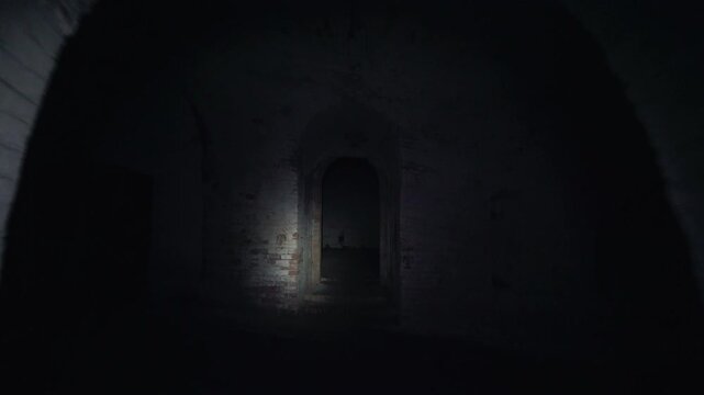 Camera moves through a dark abandoned brick corridor toward an arched doorway, with flashlight illumination revealing a decayed interior and eerie empty passage