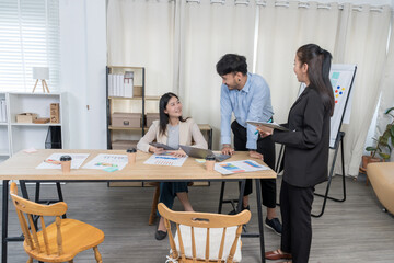 Fototapeta premium Asian Business Team Collaborating Happily:Three Asian professionals smiling while discussing ideas and reviewing documents in a modern office. Highlights positive teamwork and effective communication.