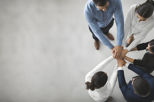 High angle view of a diverse professional business team stacking hands together in a circle, symbolizing unity, collaboration, and success in a modern office environment with copy space for text.
