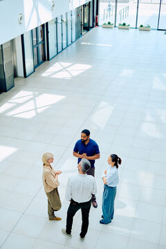Professional business people standing in a spacious modern office building lobby, actively engaging in a corporate discussion