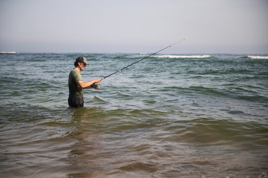 Man fishing in the sea waist-deep casting a rod on a calm coastal day