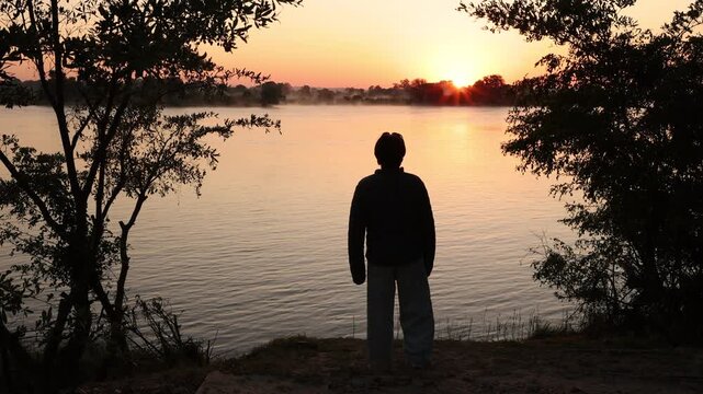 silhouette of boy looking at sunrise over the mighty Zambezi River, Zimbabwe, Africa