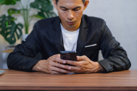 Young Man Using Smartphone at Desk with Indoor Plants in Office Environment