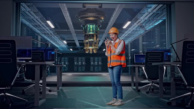 Full Body Side View Of Asian Female Engineer With Safety Helmet Using Smartphone While Standing at Futuristic Quantum Computer Data Center Control Room