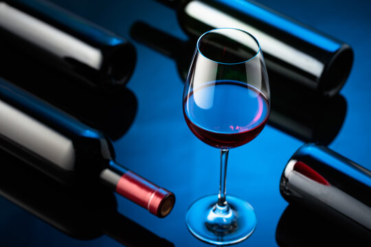 Glass and bottles of red wine on a black reflective background.