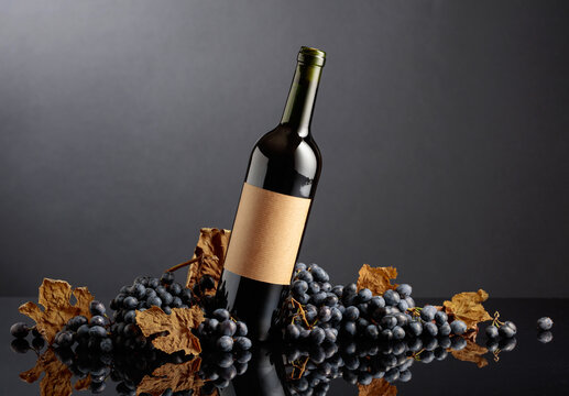 Bottle of red wine with blue grapes on a black reflective background.