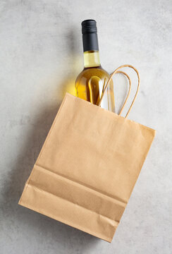 Bottle of white wine in a paper bag on a white marble background.