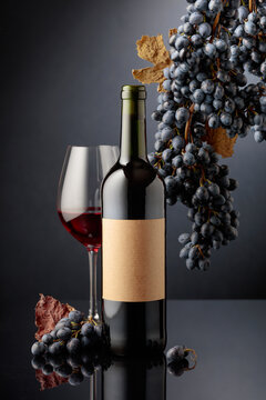 Bottle of red wine with blue grapes on a black reflective background.