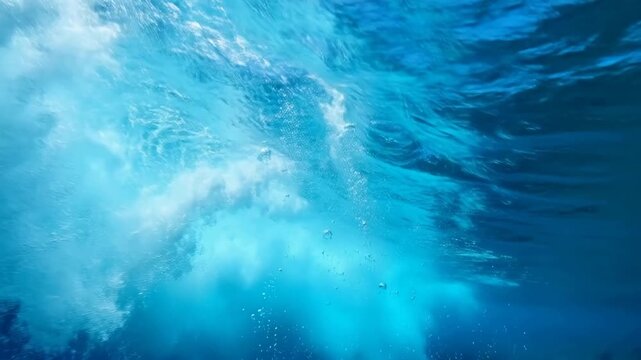 Underwater view of ocean wave breaking with bubbles rising through blue water