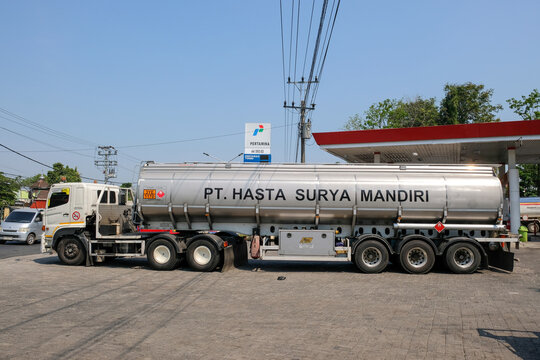 A large silver fuel tanker truck from PT. Hasta Surya Mandiri is parked at a Pertamina gas station under a clear blue sky, preparing for fuel distribution.