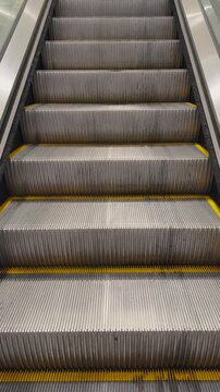 Empty escalators in modern building, symmetrical lines and metallic steps creating geometric urban pattern, 4K vertical footage
