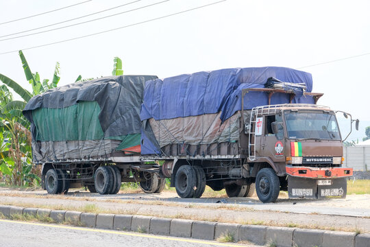 A brown Mitsubishi Fuso cargo truck with an attached heavy-duty trailer parked on the roadside, carrying a large volume of goods covered under securely tied tarpaulins.