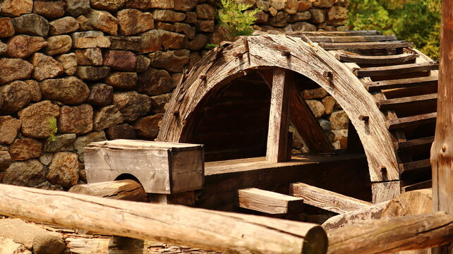 Weathered Wooden Water Wheel Detail with Stone Wall Background Capturing Rustic Historical Charm in Sunlight