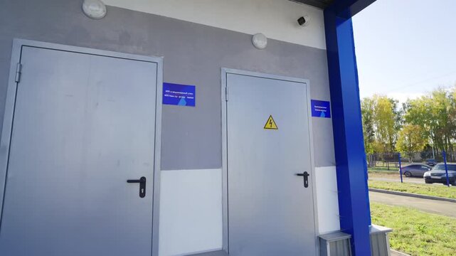 Wide stainless steel utility doors on public facility facade with blue accents. High voltage sign indicates professional electrical area