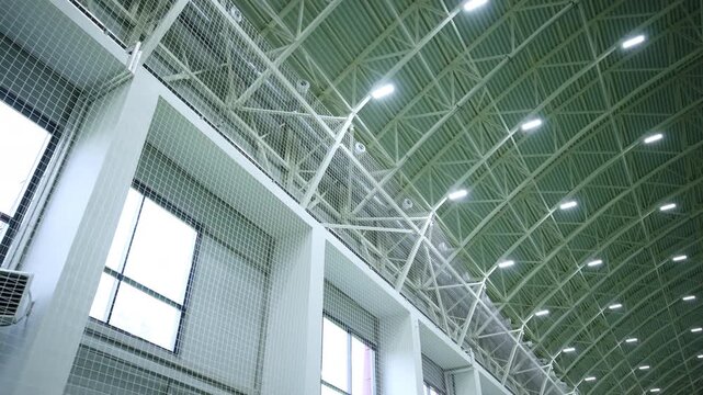 Industrial ceiling grid beams and linear rows of glowing spotlights. Functional architecture creates bright atmosphere in wide sports arena