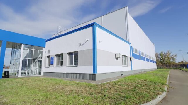 Clean corporate exterior wall with rectangular glass windows under sunny sky. Orderly green lawns and bright blue sky create fresh look